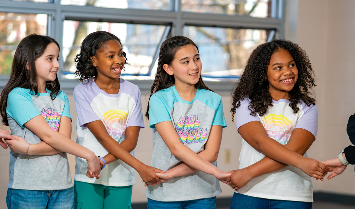 Four young girls in matching t-shirts holding hands in a line.